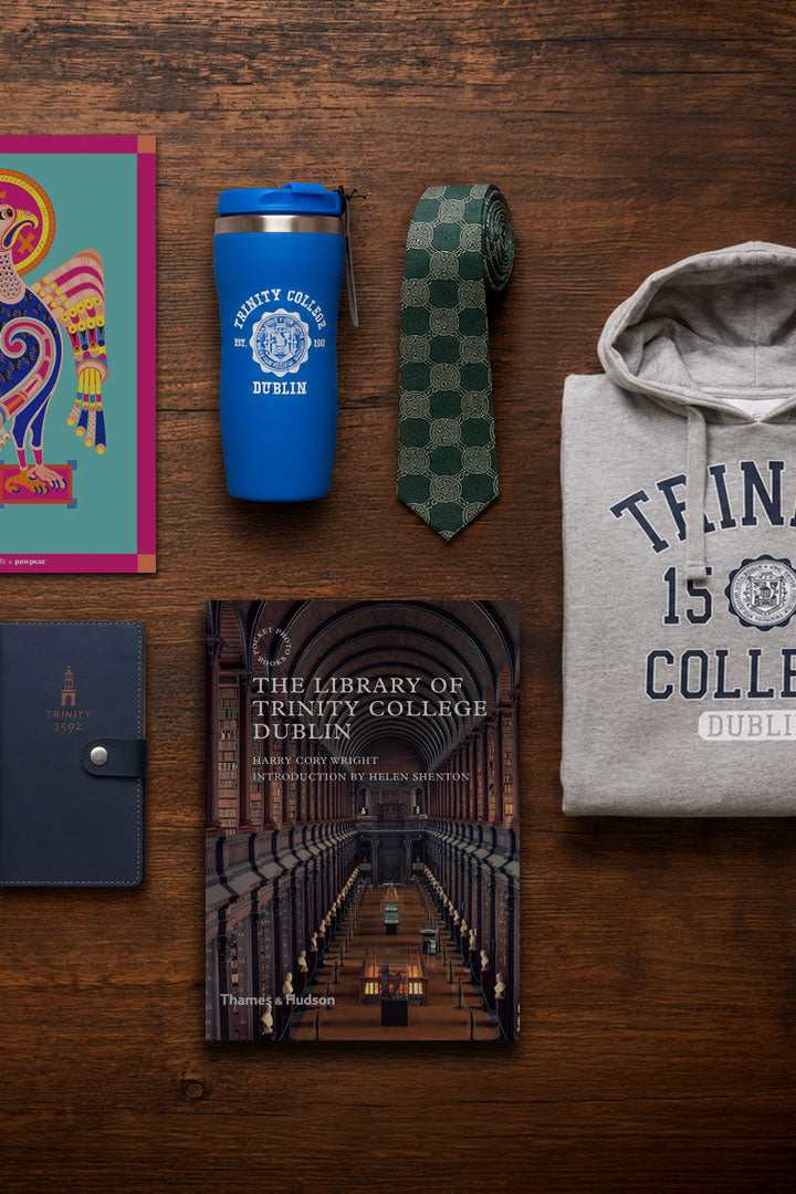 Collection of Trinity College Dublin merchandise including a tumbler, book, tie, and hoodie on a wooden surface.
