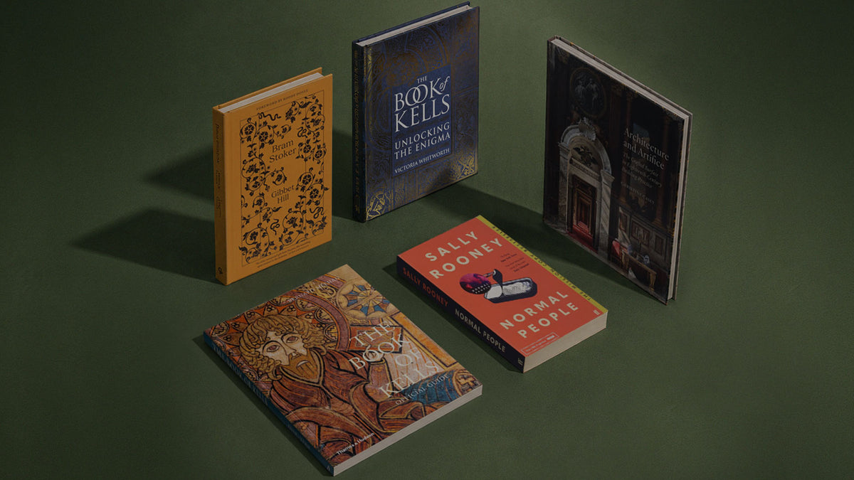 Five books arranged on a dark green surface against a matching green backdrop. The collection includes a yellow book with black floral illustration, a dark blue book titled 'Book of Kells: Envisioning the Book,' a red book titled 'Normal People' by Sally Rooney, a dark illustrated book, and a book with an ornate brown and gold cover.
