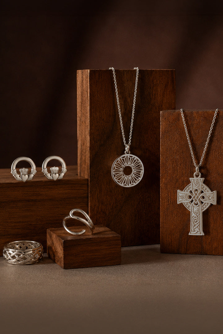 Sterling silver jewelry set displayed on dark wood blocks, featuring a Celtic cross pendant necklace, a circular sunburst pendant necklace, two ring holders, and several rings.