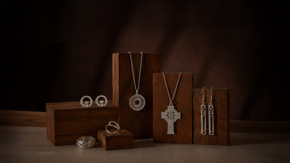 A styled jewelry display featuring silver-toned necklaces, rings, and earrings arranged on dark wooden display blocks against a dark brown background.